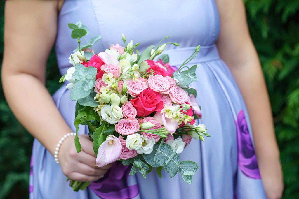 Pregnant woman in lilac summer dress holding a bouquet of colorful roses and pink calla lilies